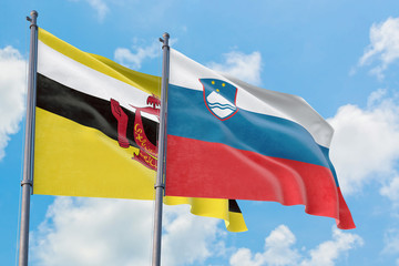 Slovenia and Brunei flags waving in the wind against white cloudy blue sky together. Diplomacy concept, international relations.