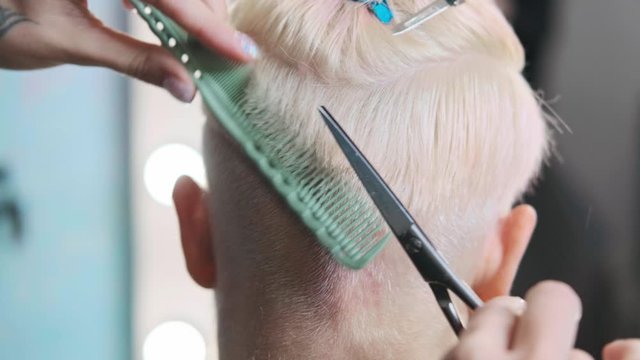 The hairdresser cuts dyed hair female client with scissors. A short pixie haircut and shaved temples . Ornament on the hair.