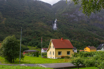 Fototapeta na wymiar A small house in the Norwegian valley, against the backdrop of a waterfall. Flam. Norway