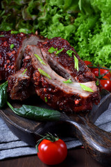 Roasted pork ribs with glazing served on the wooden board surrounded by the vegetables and herbs