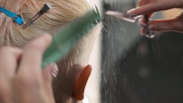 The hairdresser cuts dyed hair female client with scissors. A short pixie haircut and shaved temples . Ornament on the hair.