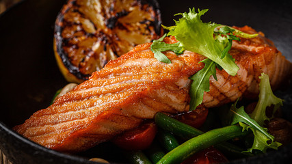 European cuisine in Ukrainian style. A large steak of red salmon fish, with mushrooms, asparagus, cherry tomatoes and fried lemon. Serving meals in a rustic restaurant.