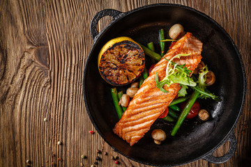 European cuisine in Ukrainian style. A large steak of red salmon fish, with mushrooms, asparagus, cherry tomatoes and fried lemon. Serving meals in a rustic restaurant.