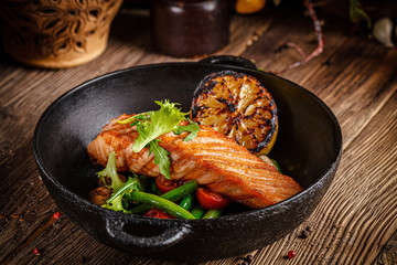 European cuisine in Ukrainian style. A large steak of red salmon fish, with mushrooms, asparagus, cherry tomatoes and fried lemon. Serving meals in a rustic restaurant.
