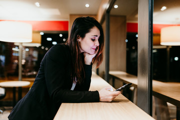 young woman using mobile phone in a cafe or restaurant indoors. Technology and lifestyle