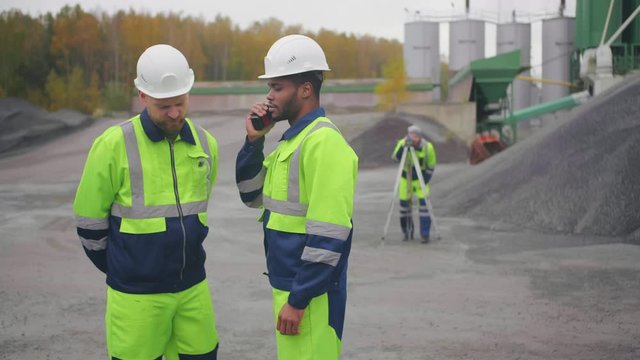 Multicultural industrial workers using walkie talkie standing outdoors at asphalt concrete factory