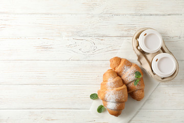 Tasty croissants and cups with coffee on wooden background, top view
