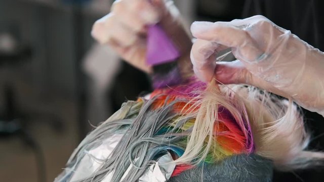 Hairdresser colorist puts paint on the hair with a brush. A short haircut, shaved temple, ornament on the hair. Coloured hair dye in the salon.