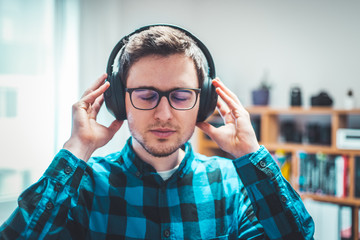 Enjoying music at home: Young Caucasian man is listening to music with headphones. Blue checked...