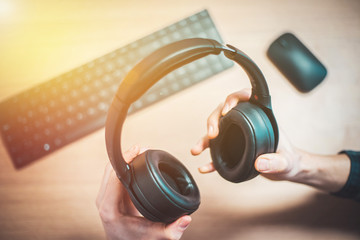 Naklejka premium Workspace audio concept: Holding black wireless headphones, workspace in the blurry background