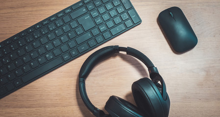 Workspace media concept: Black wireless headphones, keyboard and mouse on wooden desk