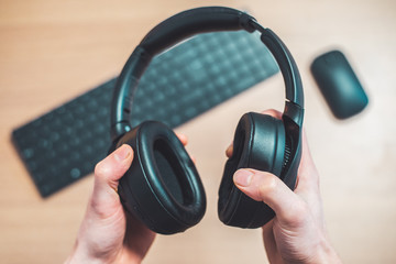 Obraz na płótnie Canvas Workspace audio concept: Holding black wireless headphones, workspace in the blurry background