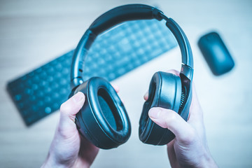 Obraz na płótnie Canvas Workspace audio concept: Holding black wireless headphones, workspace in the blurry background