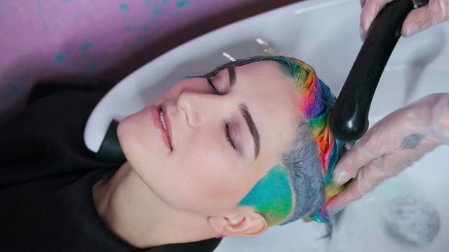 The hairdresser washes the head of a female client in the salon. Hair dyed in different colors.