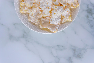 Frappe di carnevale, dessert italiano cucinato a febbraio, sul piatto bianco e fondo di marmo, spazio del testo