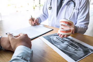 Professional Dentist showing  jaw and teeth the x-ray photograph and discussing during explaining the consultation treatment issues with patient and writing history list on report - obrazy, fototapety, plakaty