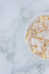 Frappe di carnevale, dessert italiano cucinato a febbraio, sul piatto bianco e fondo di marmo, spazio del testo