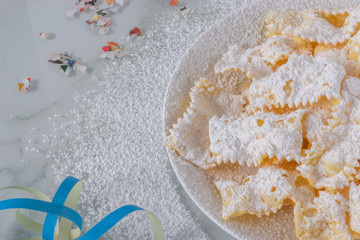 Frappe di carnevale, dessert italiano cucinato a febbraio, sul piatto bianco e fondo di marmo, spazio del testo