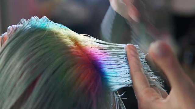 The hairdresser cuts dyed hair female client with scissors. A short pixie haircut and shaved temples . Ornament on the hair.