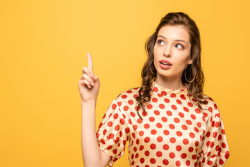 thoughtful young woman looking up while showing idea gesture isolated on yellow