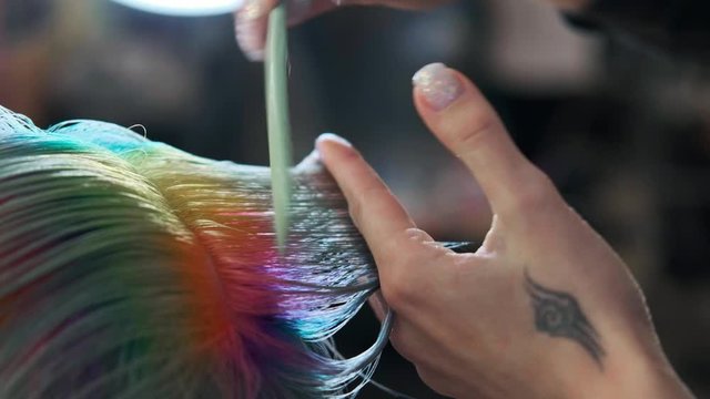 The hairdresser cuts dyed hair female client with scissors. A short pixie haircut and shaved temples . Ornament on the hair.