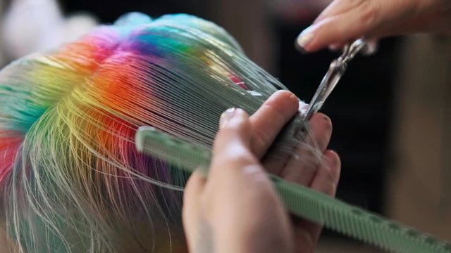 The hairdresser cuts dyed hair female client with scissors. A short pixie haircut and shaved temples . Ornament on the hair.