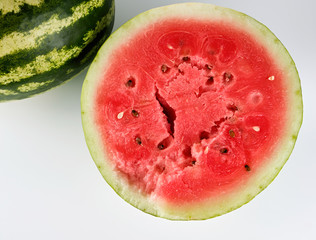 half ripe watermelon with red juicy pulp and seeds and a whole green