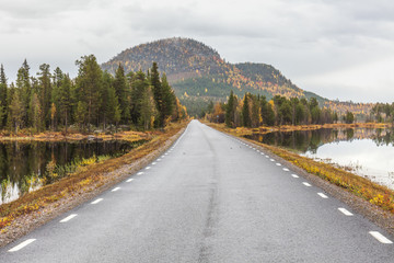 The road running along the lake at sunset goes into the mountains.