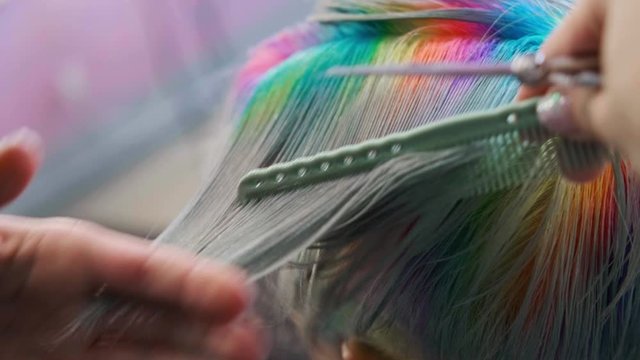 The hairdresser cuts dyed hair female client with scissors. A short pixie haircut and shaved temples . Ornament on the hair.