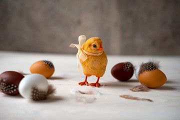 Decorative easter chicken with bow and eggs on a white and gray wooden background.