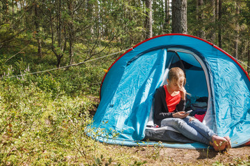 Girl using smartphone sitting in a camping tent during summer holidays