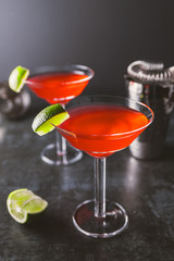 Red cocktail with lime in Martini glass on a table.