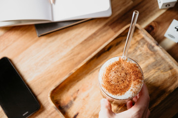 Cup of latte served with glass tube on a wooden  work desk. Coffee break concept.