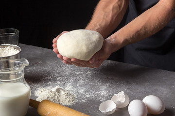 A man is making a dough for varenyky or dumplings, with meat, onions and bacon. Man in a black apron without face. Making dough by male hands at bakery Stone table close-up photo 