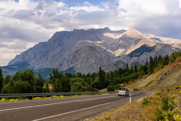 Panoramic view of the mountain with car on the road, forest and cloudy sky in summer