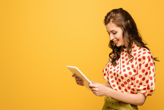 young woman smiling while using digital tablet isolated on yellow