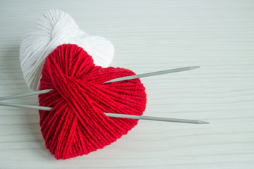 A ball of red yarn in the shape of a heart with spokes on a white wooden background with space for copying