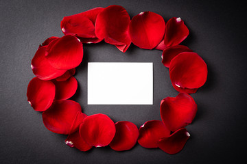 Red roses petals with a gift card to write on it on a black background. Concept of Valentine's Day, anniversary or mother's day.