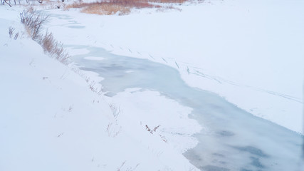 Thin ice melts on the river in early spring. Snowy riverbank with dry grass. Pure and clean nature concept