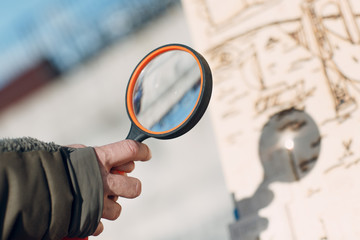 Magnifying glass burning picture. Loupe in hand and sunbeam.