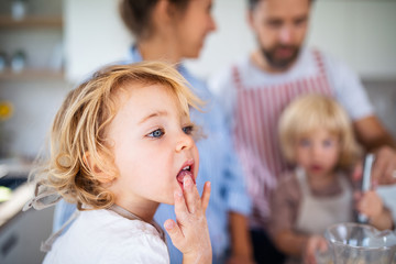 Small girl with family indoors in kitchen, cooking.