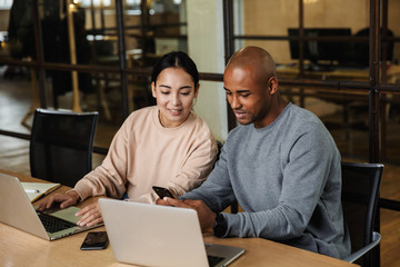 Image of multiethnic young coworkers working on laptops in office