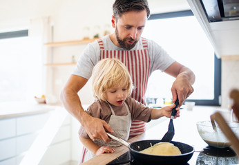 A small boy with father indoors in kitchen making pancakes.