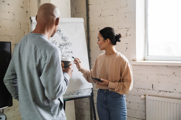 Obraz premium Image of multiethnic young coworkers standing by flipchart in office
