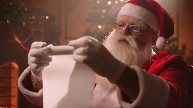 Portrait of Santa Claus rolls up a scroll on Christmas eve and checks the list of children to whom gifts are prepared. Fantastic atmosphere
