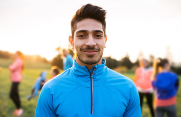 A portrait of young man with large group of people doing exercise in nature.