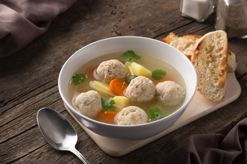 Bowl of chicken soup. Homemade Chicken soup with meatballs, potatoes, carrots and parsley on a rustic background. Served on an old wooden table with croutons. Close-up shot.  