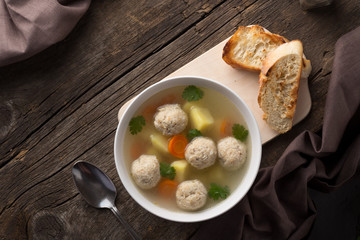 Bowl of chicken soup. Homemade Chicken soup with meatballs, potatoes, carrots and parsley on a rustic background. Served on an old wooden table with croutons. View from above. Top view. Close-up shot.
