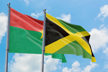 Jamaica and Burkina Faso flags waving in the wind against white cloudy blue sky together. Diplomacy concept, international relations.