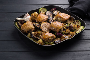 Chicken thighs with grilled vegetables. Chicken served in a frying pan on an old wooden table. Chicken with lime, zucchini, eggplants, onions and garlic. Close-up shot. Free space for text.